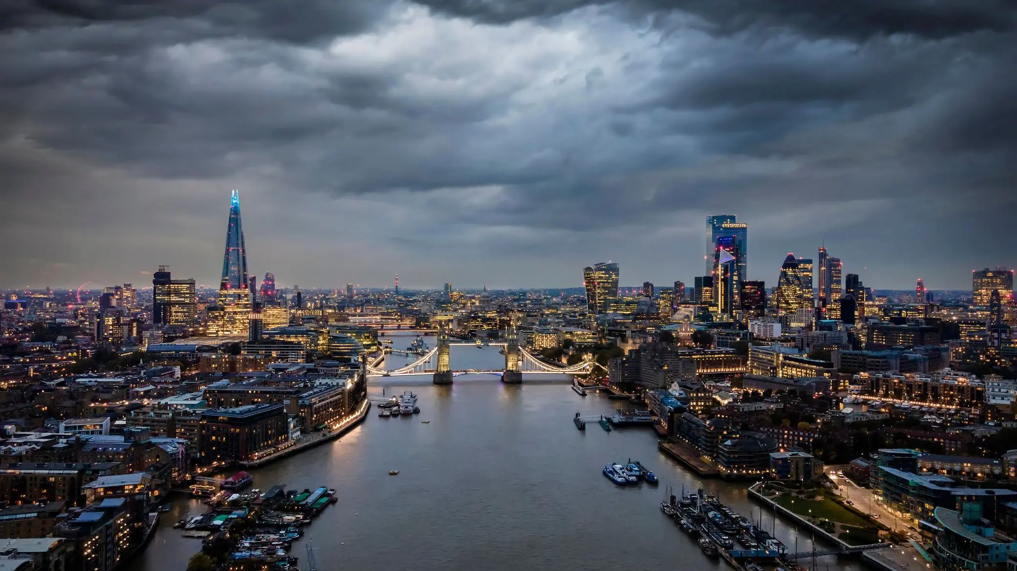 Elevated, moody view of the illuminated skyline of London, United Kingdom, with a cloudy sky at dusk.