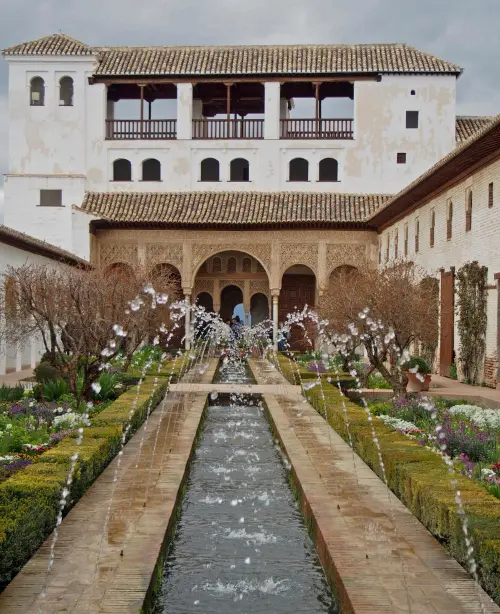 The Alhambra fortress in Granada, featuring red stone walls, Moorish arches, and hilltop views overlooking the city and mountains.