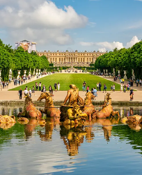 Expansive formal gardens at the Palace of Versailles in Versailles, featuring geometric hedges, fountains, and tree-lined pathways under a clear sky
