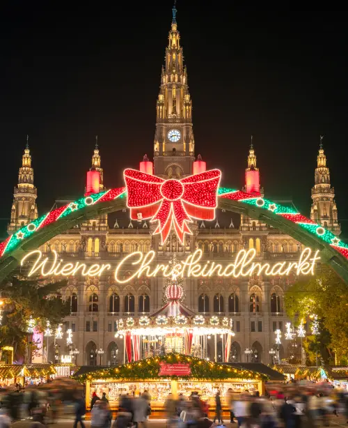Christmas market in Vienna at night with glowing lights, festive stalls, decorated trees, and crowds enjoying the holiday atmosphere