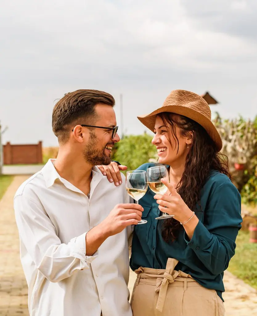 Young smiling couple tasting wine at winery vineyard - Friendship and love concept with young people enjoying harvest time
