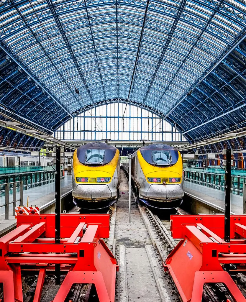 Two Eurostar high-speed trains with distinctive yellow and silver noses sit side by side at London St Pancras International station, beneath the station's sweeping Victorian arched glass and iron roof.