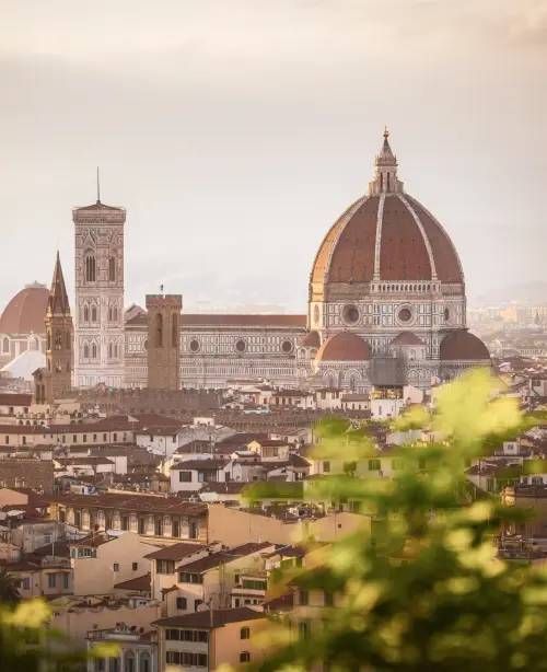 Panoramic view of Florence featuring the red-tiled Duomo dome, historic buildings, and the Arno River flowing through the city.