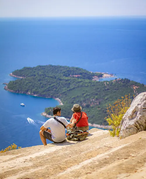 Friends hiking along scenic trails in Dubrovnik, overlooking the Adriatic coastline and historic stone walls under clear skies.