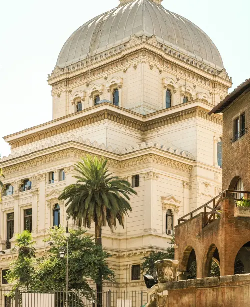 Exterior of the Great Synagogue of Rome in Rome, featuring a large square dome, neoclassical façade, and decorative architectural details along the Tiber River.
