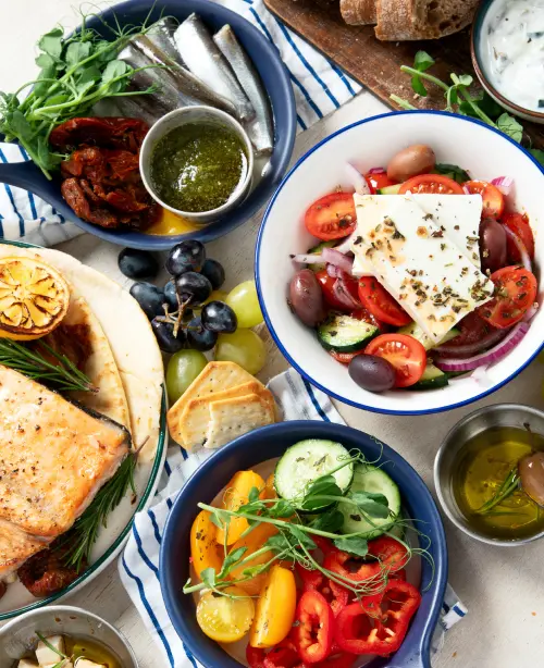 Colorful Mediterranean dishes served on a table with olive oil, herbs, fresh ingredients, and grilled meats.