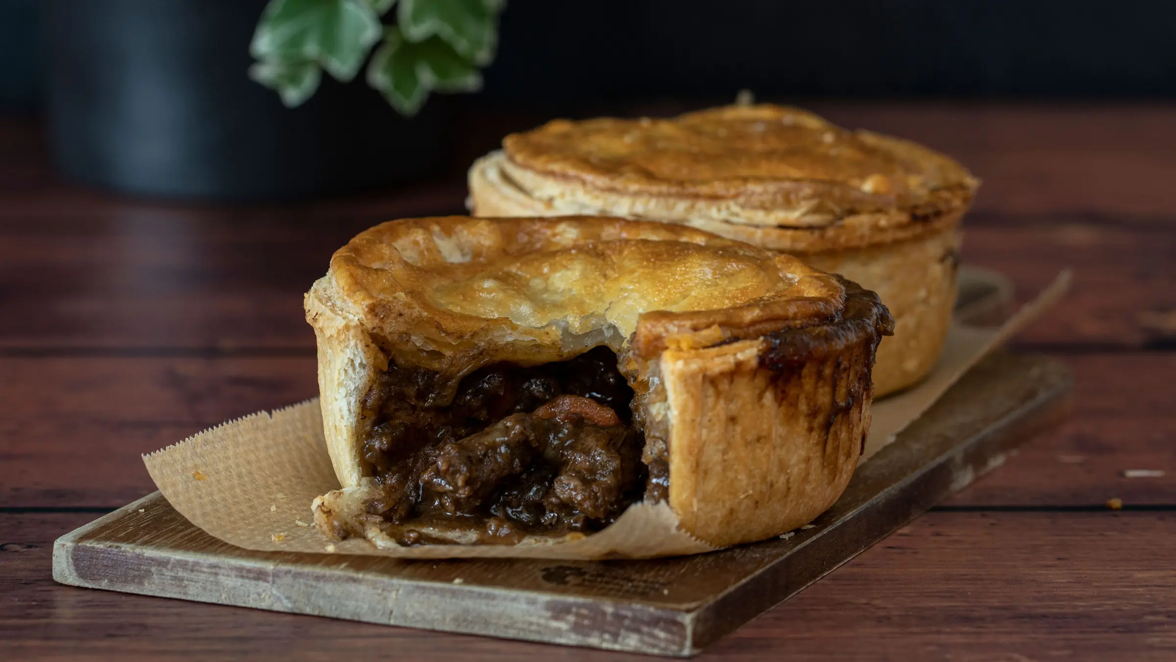 A close-up of two meat pies on a wooden board.