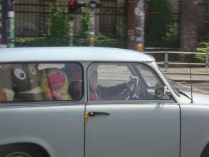An Ostalgie trifecta: A Trabant stuffed with East German plushes, with the Sandmännchen riding beside the driver, and an Ampelmännchen in the background