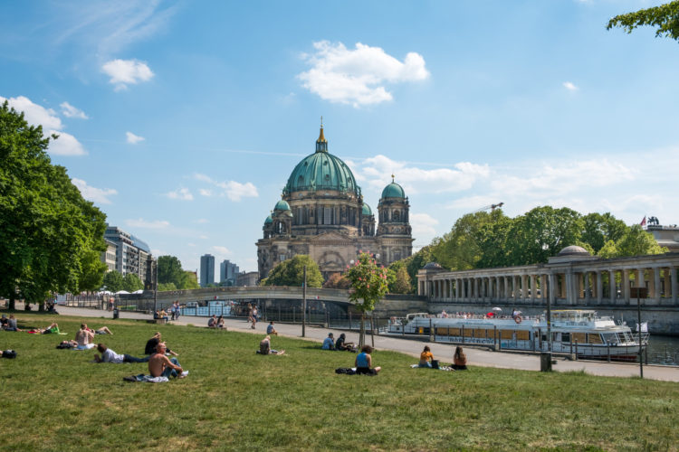 Berlin, Germany - may 23, 2017:People relaxing on meadow in Monbijoupark on a sunny day in Berlin with the Berlin cathedral and tourist boat in background.