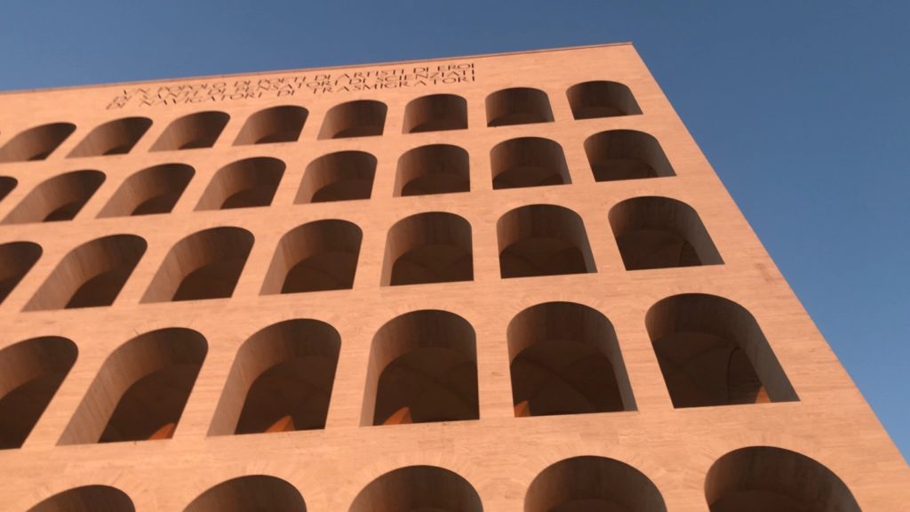 Looking up at the arches of the Palazzo della Civiltà Italiana. bathed n late afternoon sunlight, against a cloudless blue sky.