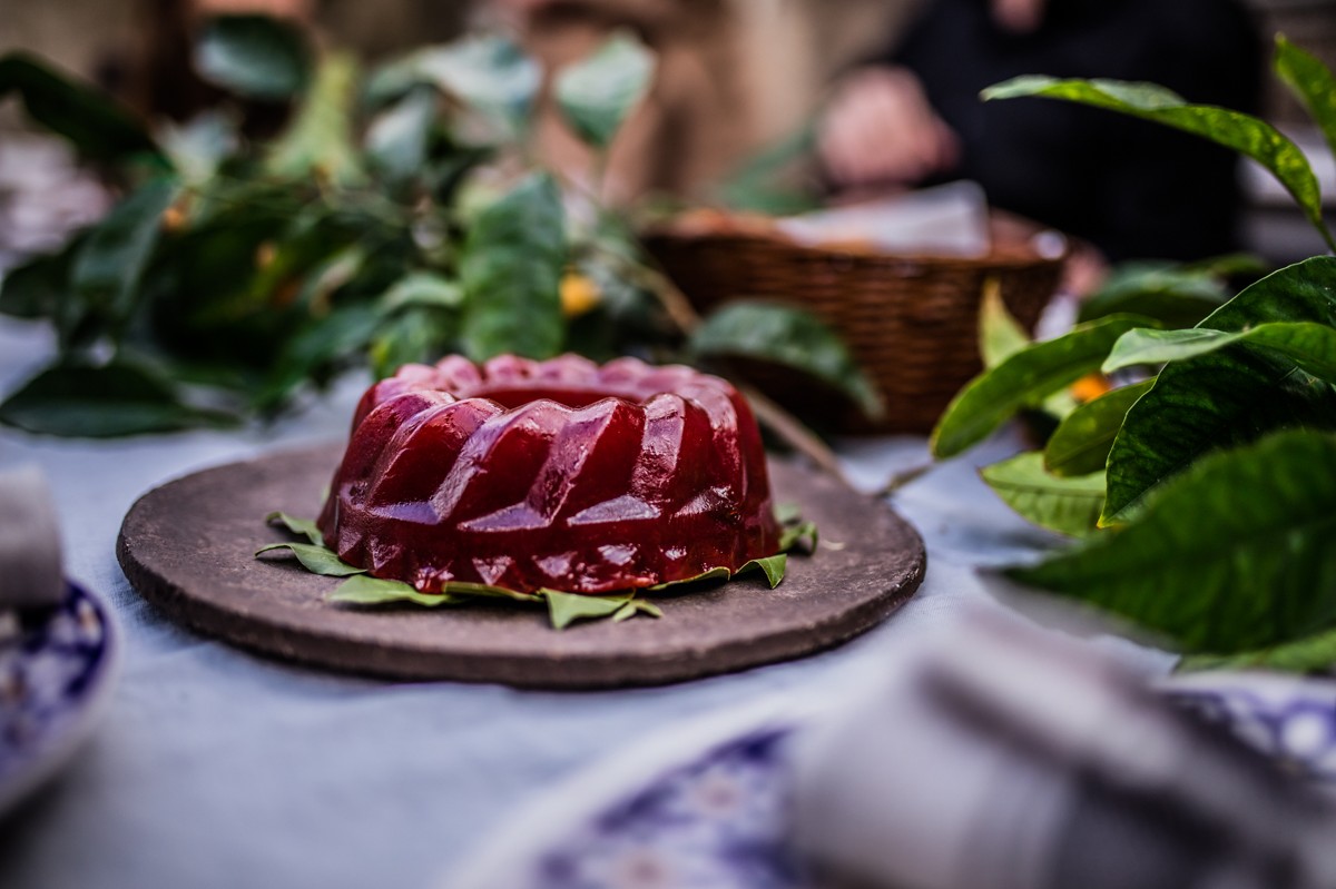 A red round jelly-like dessert served on a bed of bay leaves on a tray. 