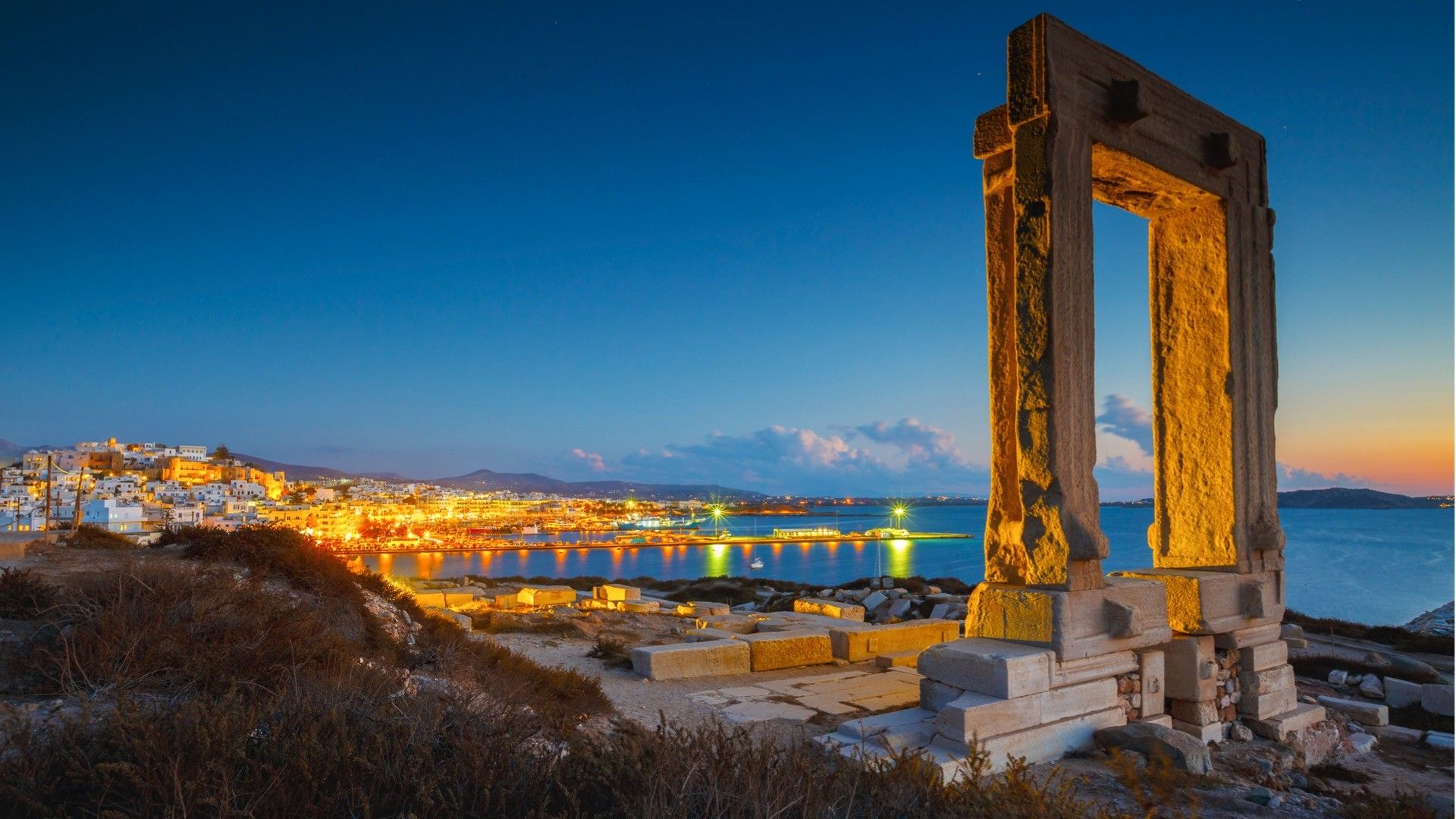 This image shows Portara in the blue hour with the view of Naxos Town in the background. 
