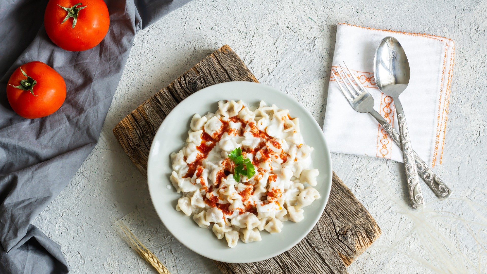 This is a top-down photo of a plate filled with manti, topped with tomato sauce and garlic-yogurt sauce. 