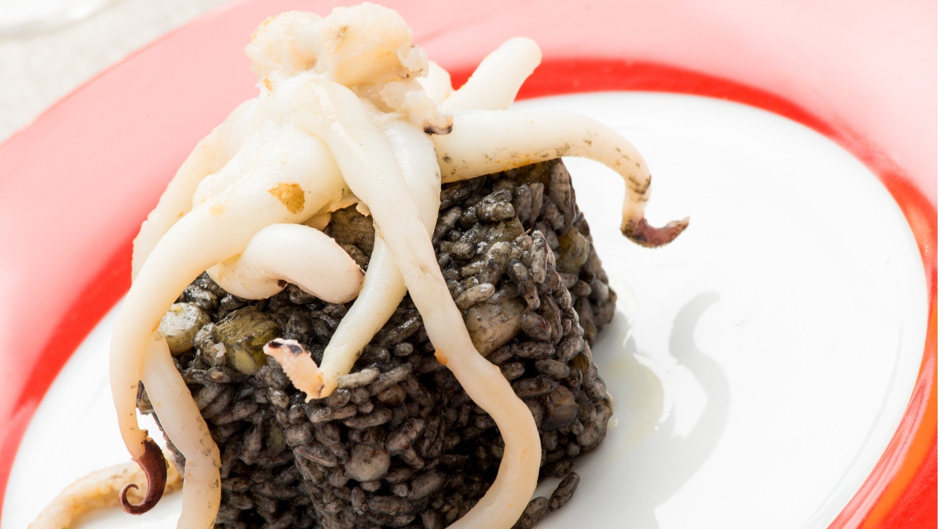 This is a close-up of a dish of black risotto with cuttlefish on top of it. This type of Croatian risotto is the most famous in the country. 