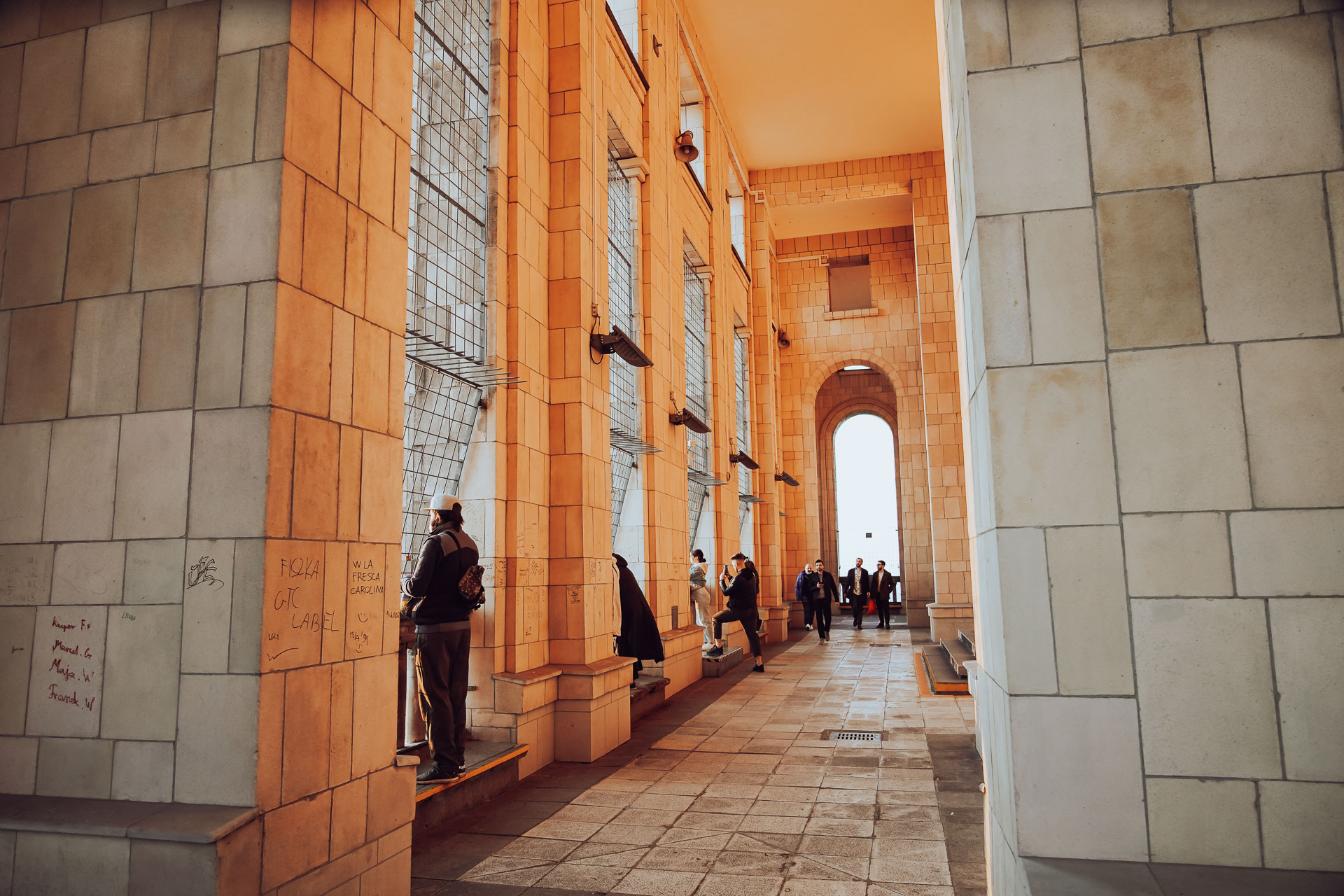 A corridor of the observation terrace on the 30th floor of the Palace of Culture and Science in Warsaw, Poland. High ceiling archways filled with evening light with a few visitors enjoying the view.