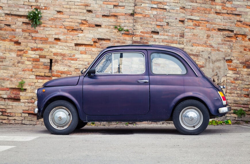 This image shows a vintage Fiat 500 parked in front of a brick wall. Fiat 500 tours in Italy are among the best classic car tours in Europe.