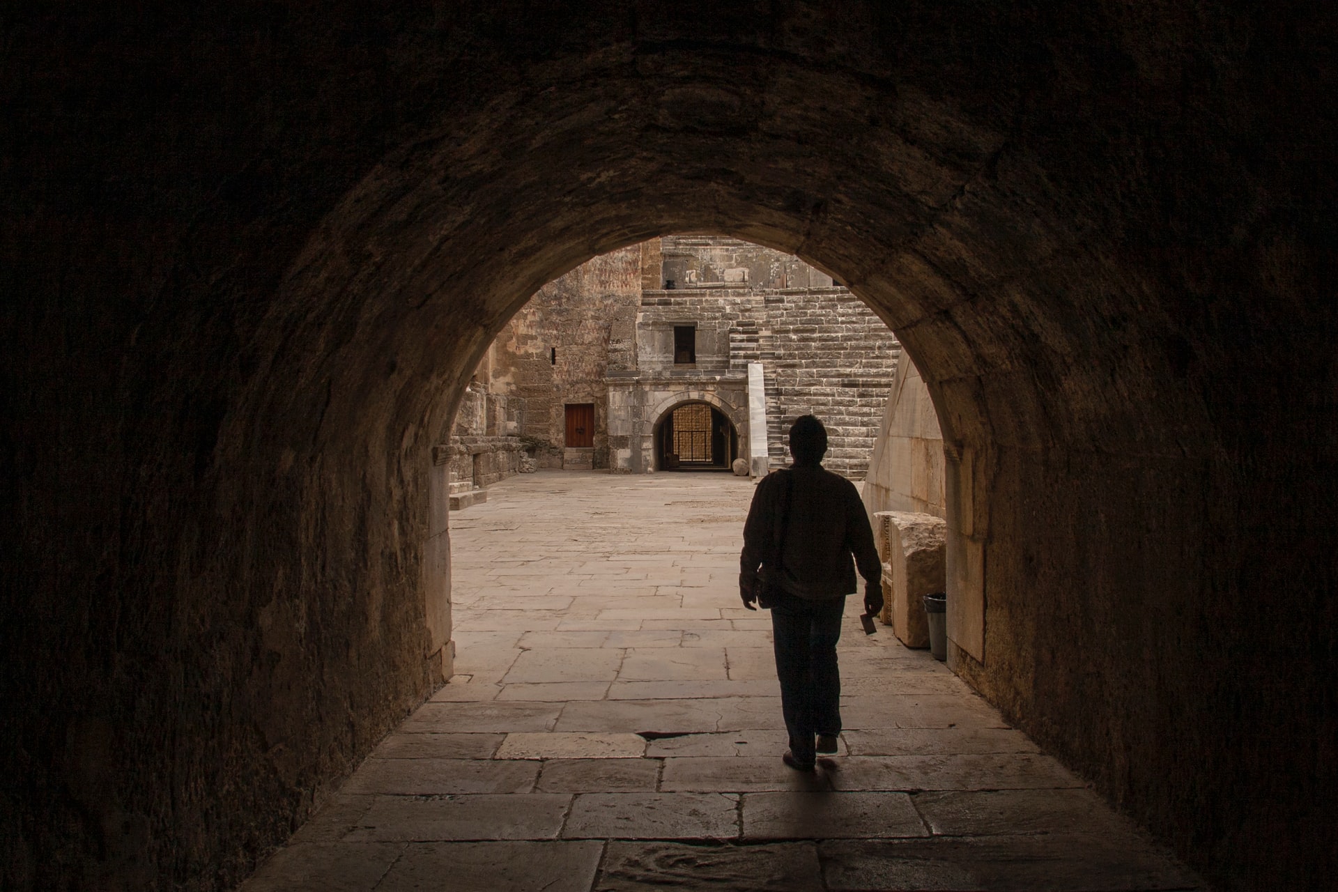 Cette image montre un homme marchant sous un passage voûté du théâtre Aspendos.