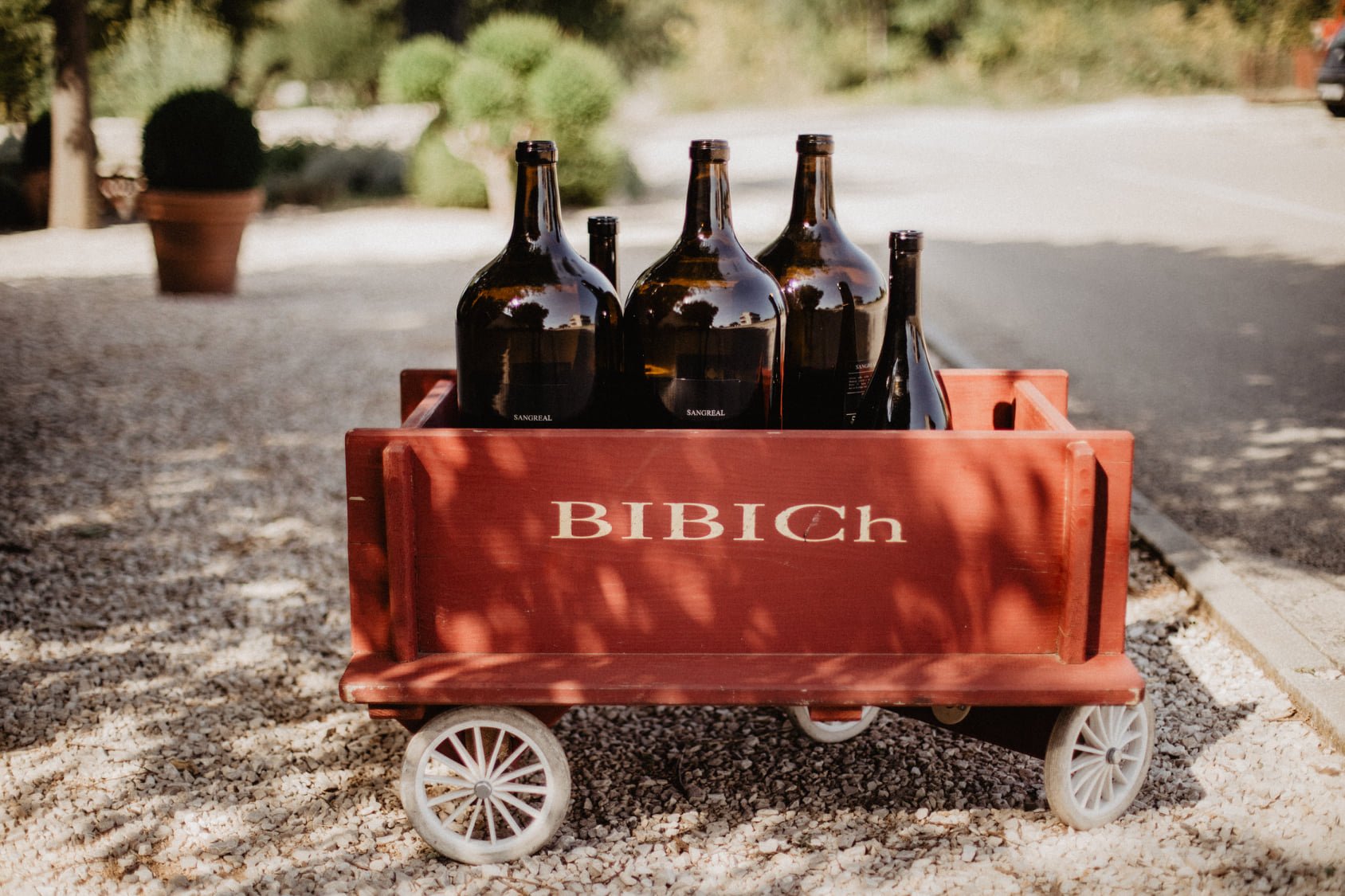 This image shows five brown glass bottles of varying sizes inside a small wooden cart that reads Bibich, one of the top wineries in Split. 