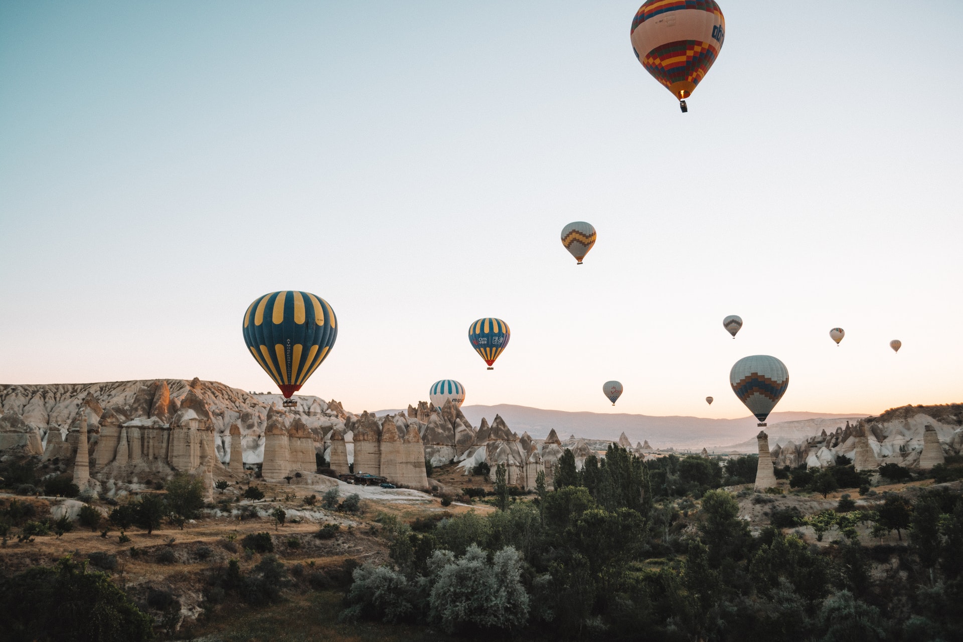 This is a panoramic shot of the impressive rock formations in Goreme with hot-air balloons flying over them.