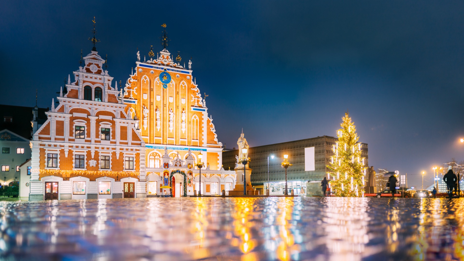 This image shows the facade of two beautiful buildings in Riga. There's also a Christmas tree and people walking. 