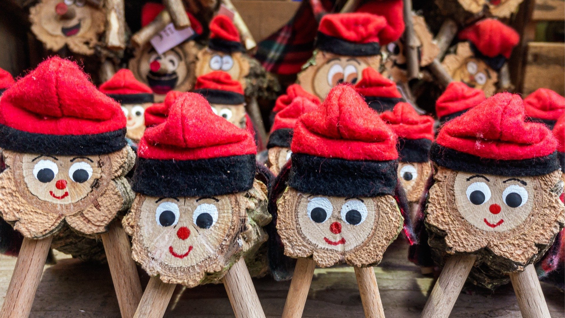 A close up of several Tio de Nadal toys: smiling faces wearing red hats, carved on wood. 