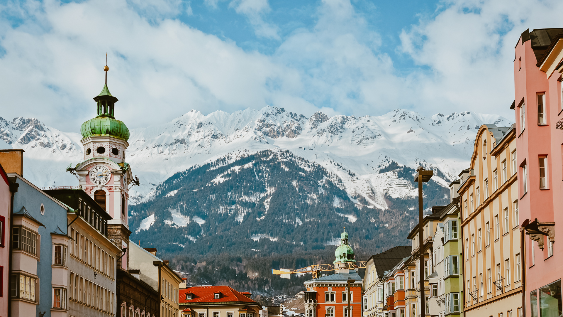 View looking up at a snowy mountain in the background with old buildings of a main square in Innsbruck, Austria in the foreground. One clocktower stands out on the left.