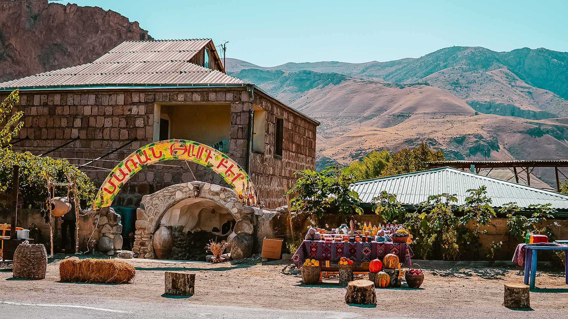 Vedere a unei crame din Areni, Armenia, cu munți în fundal și tarabe cu produse de casă în față.