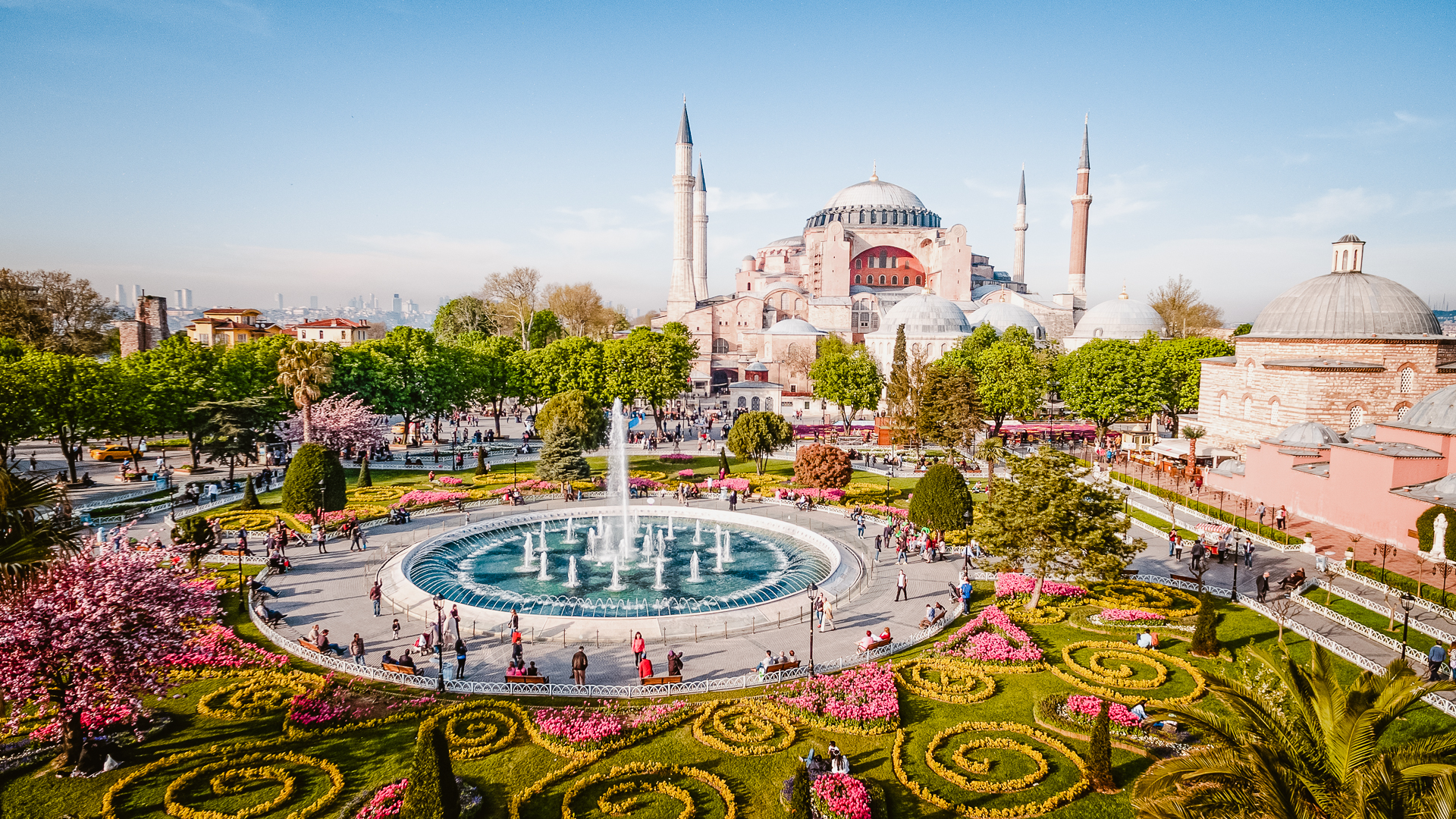 Aerial view of Hagia Sophia in Istanbul, Turkey with a huge fountain, fresh colored grass and intricate gardening work in a city park.