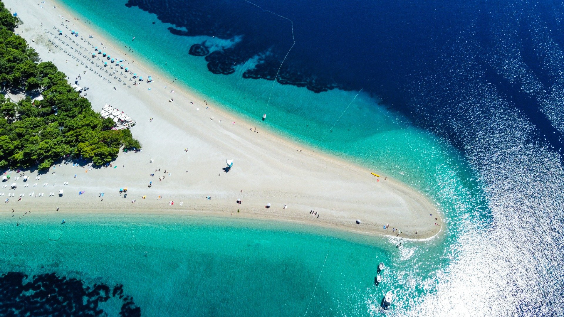 Esta é uma foto de drone de cima para baixo da Praia Zlatni Rat.  Há um pedaço estreito de terra de areia branca e águas insanamente azul-turquesa. 