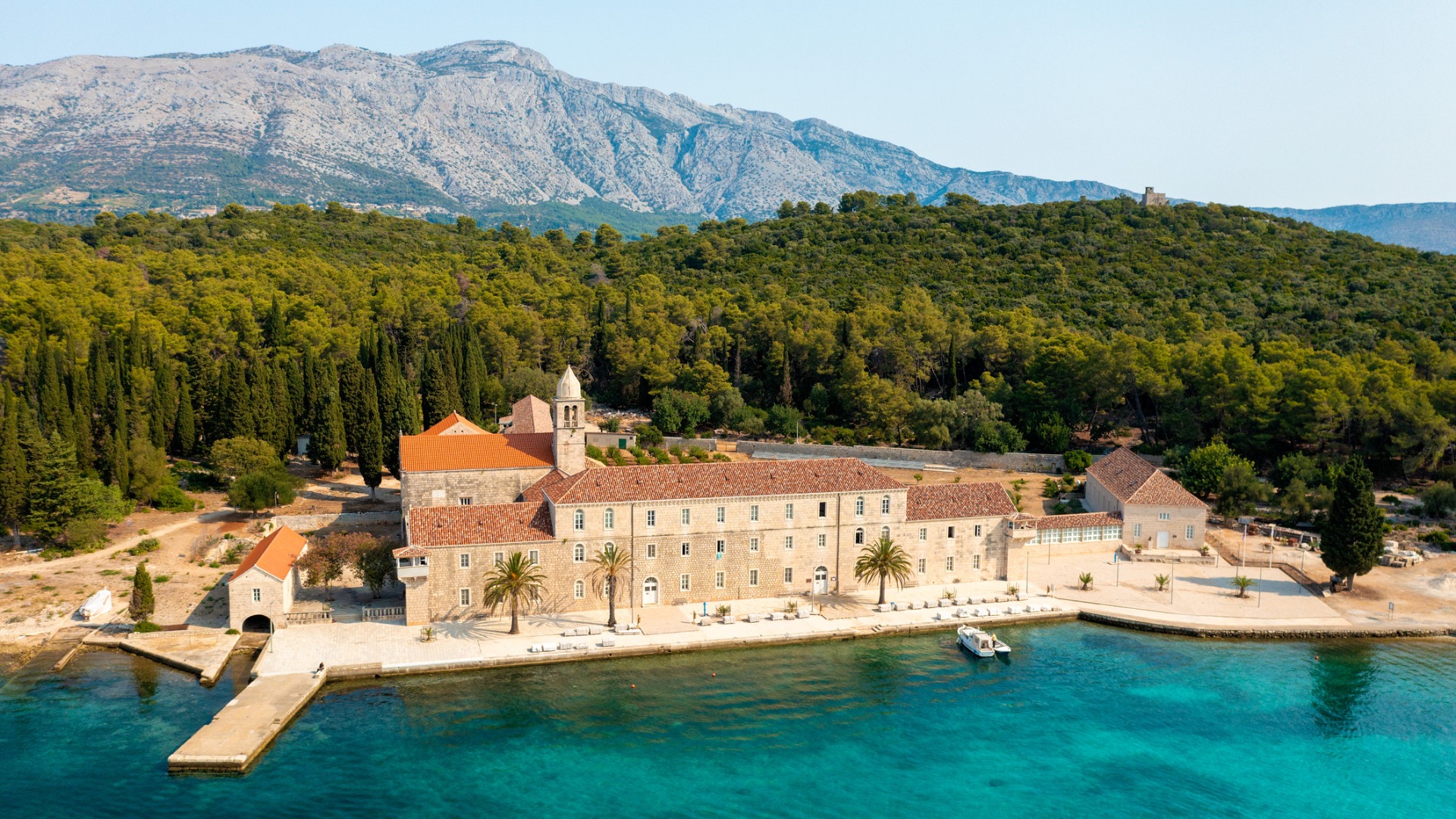 This image shows the Franciscan monastery surrounded by a thick forest and insanely clear turquoise waters.