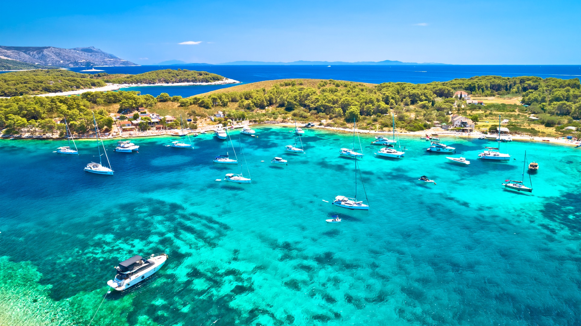 This image shows the transparent turquoise waters of Marinkovac Island. There are many sailing boats.