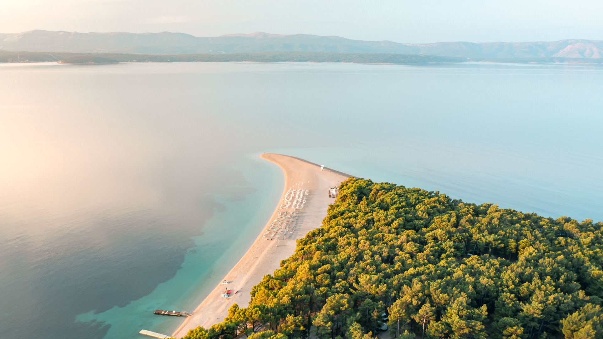 This is an aerial view of Zlatni Rat Beach, one of the best Croatia beaches. There's a strip of white sand with a thick forest behind it.