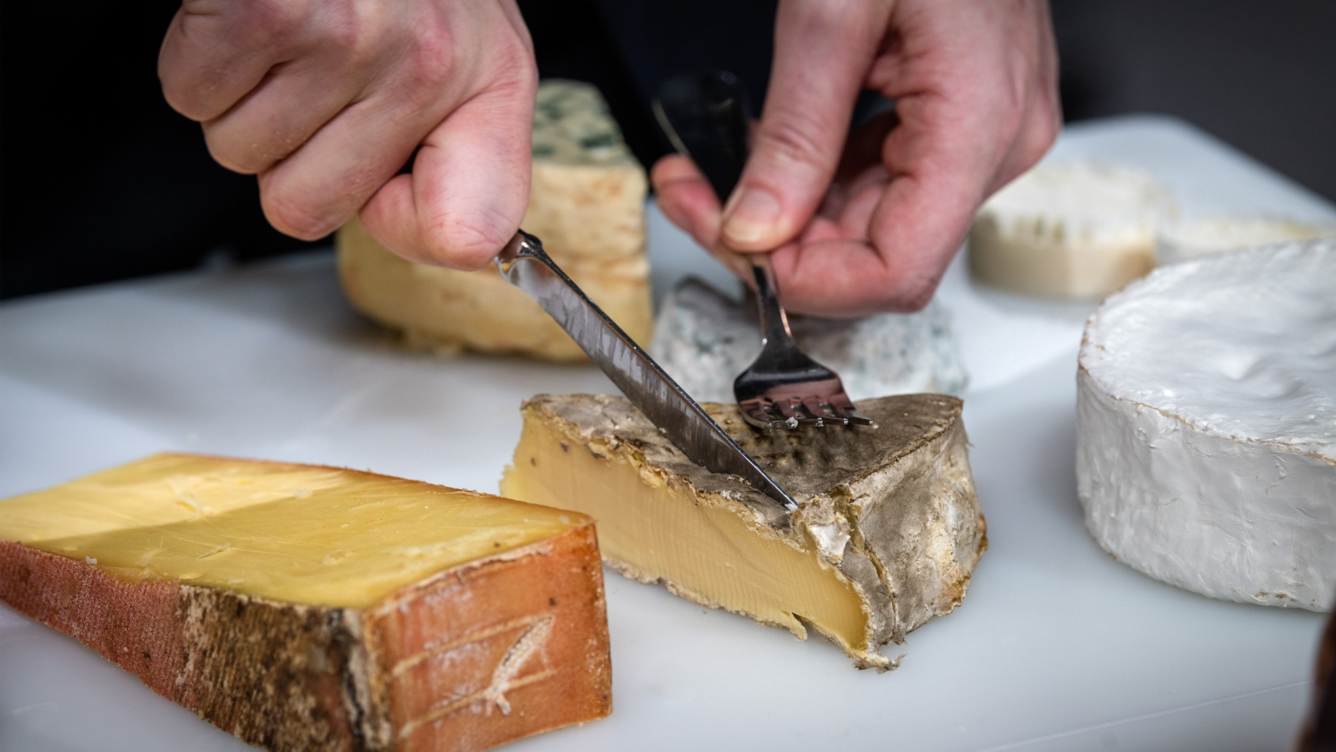 This is a close-up of a man cutting cheese in a plateau of various types of French cheese. 
