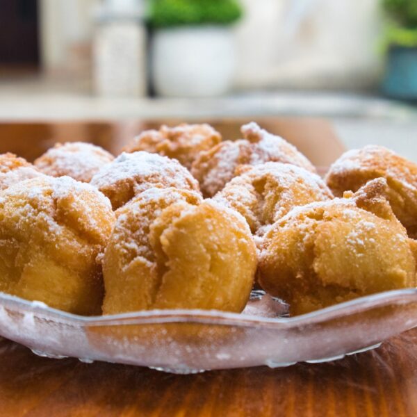 This image shows a glass bowl filled with Croatian fritule.