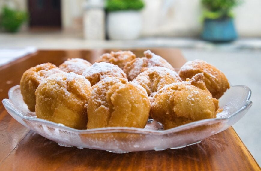 This image shows a glass bowl filled with Croatian fritule.