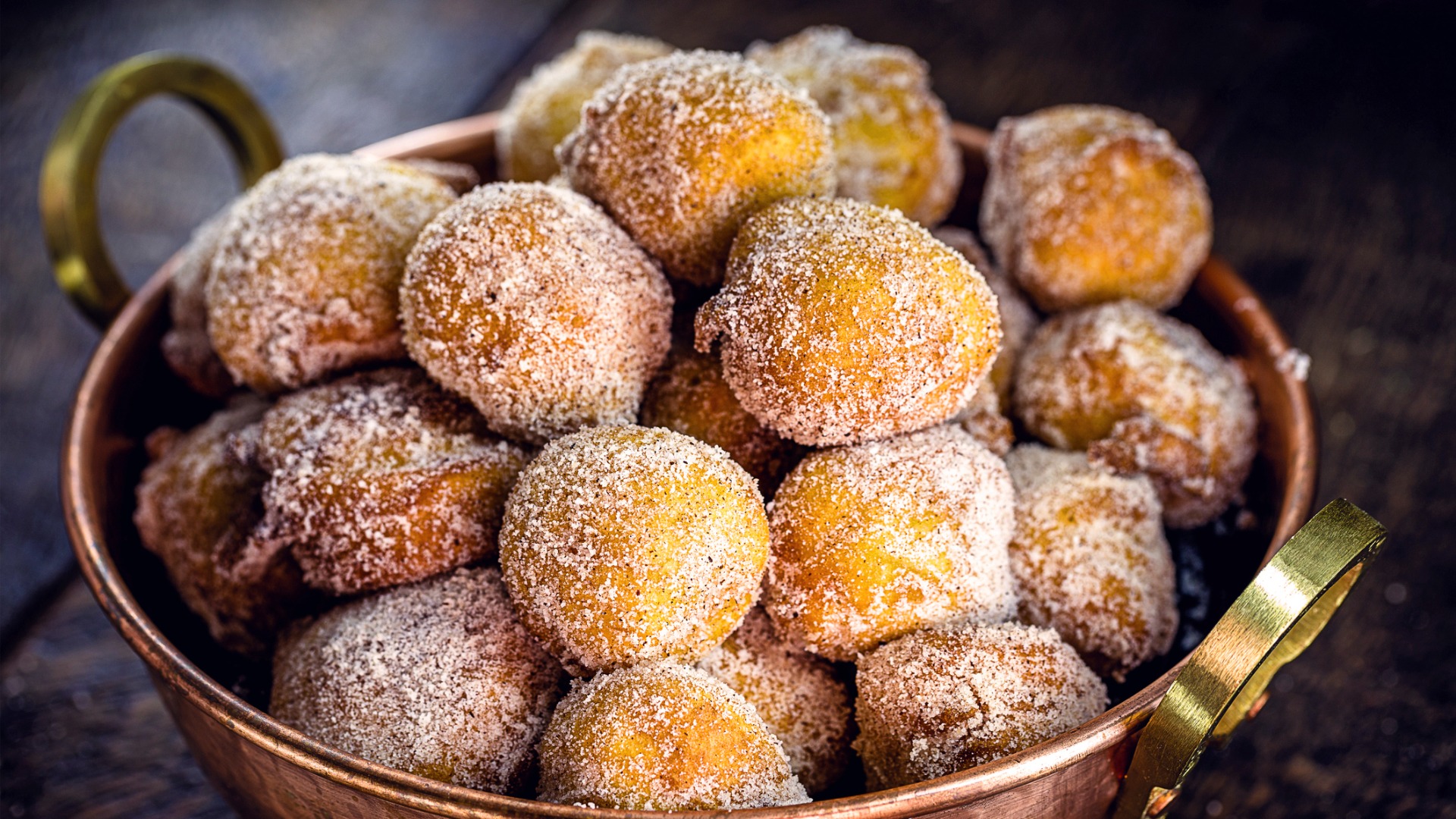 This is a close-up of a bowl filled with fritule - round dough balls covered in sugar and cinnamon.