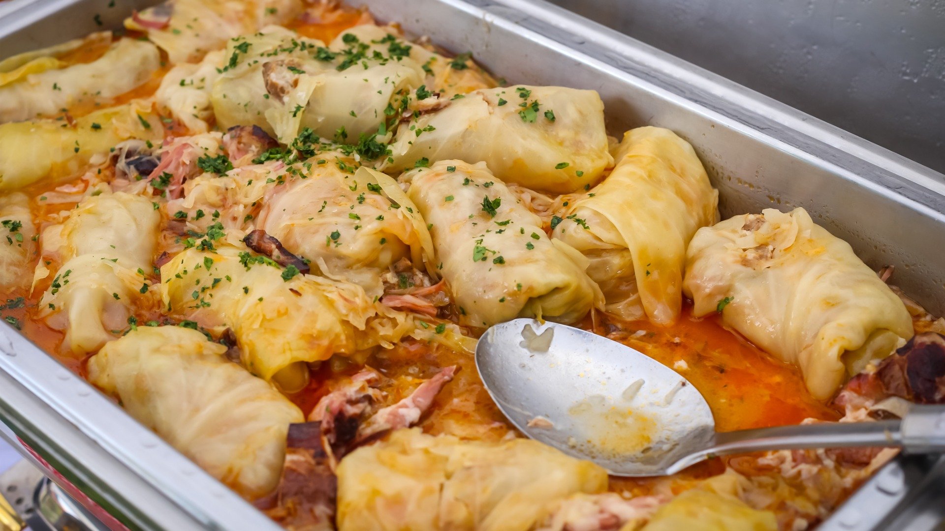 This is a close-up of a baking dish filled with sarma in tomato sauce. 