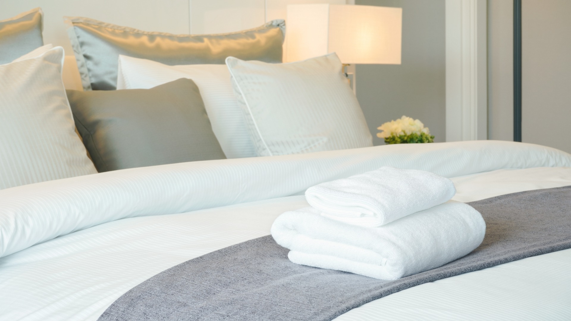 This is a close-up of a hotel bedroom. The bed is set and there are two fresh towels on the bed. 