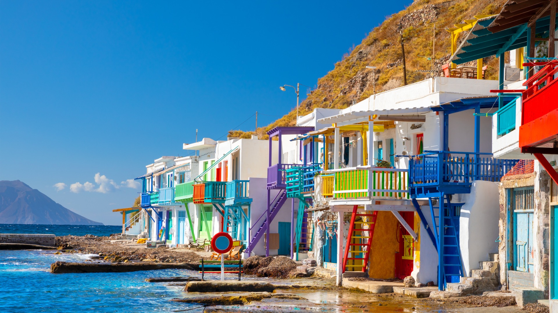 This is a photo of the distinct buildings built by the water in Klima Village. The buildings are whitewashed with colorful doors, shutters, and staircases. 