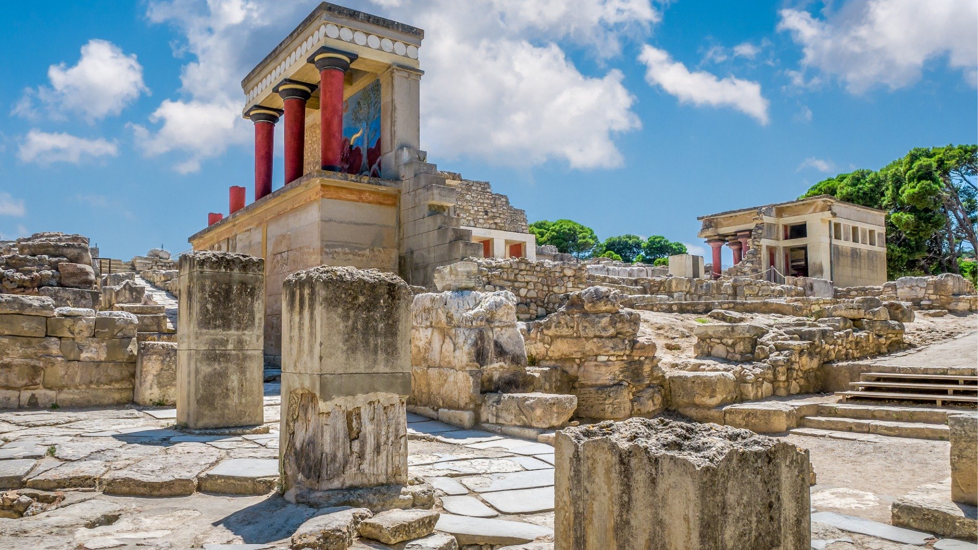 This image shows the ruins of Knossos Palace. One of the ancient buildings has bright red-colored columns. 