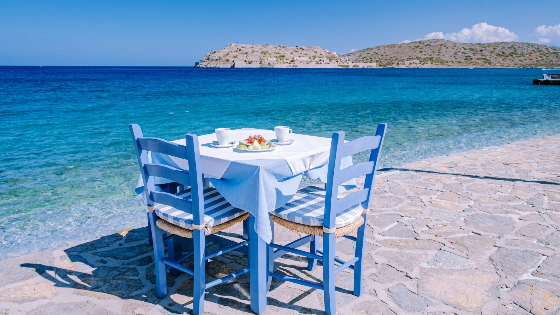This image shows a blue table with blue chairs by the sea. 