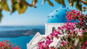 This image shows a blue-domed church in the foreground and the Santorini Volcano in the background.