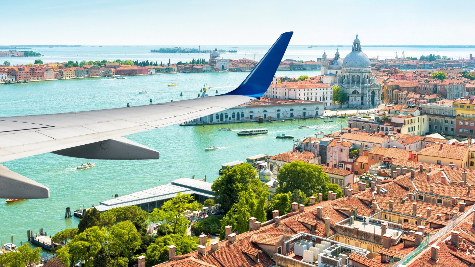 This image shows the wing of a plane as it flies over Venice, a city you must include in your itinerary when planning a trip to Italy and Greece. 