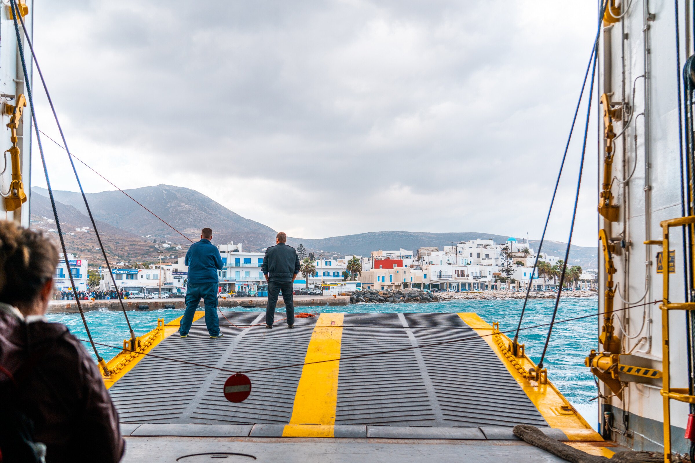 This image shows two people standing at the half open ferry door as the ferry approaches Parikia Port in Paros. 