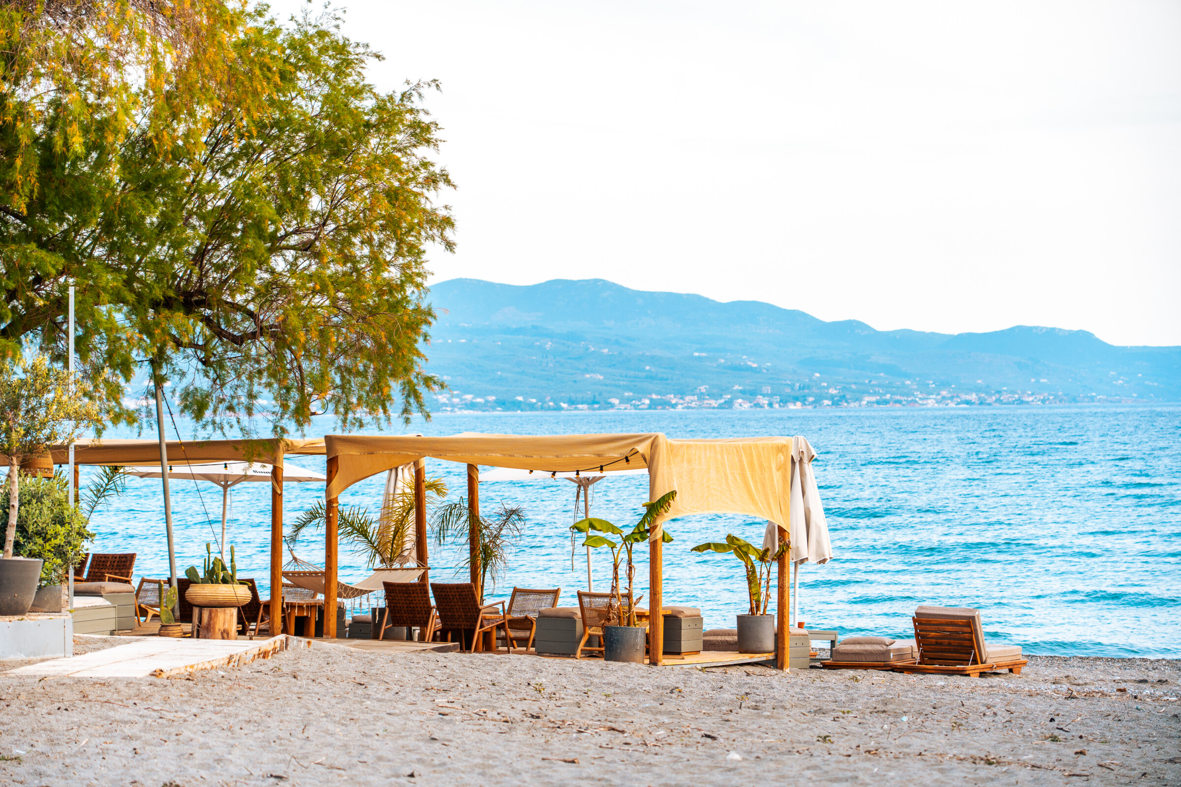 This image shows a beach café right by the calm sea and mountains in the background. 