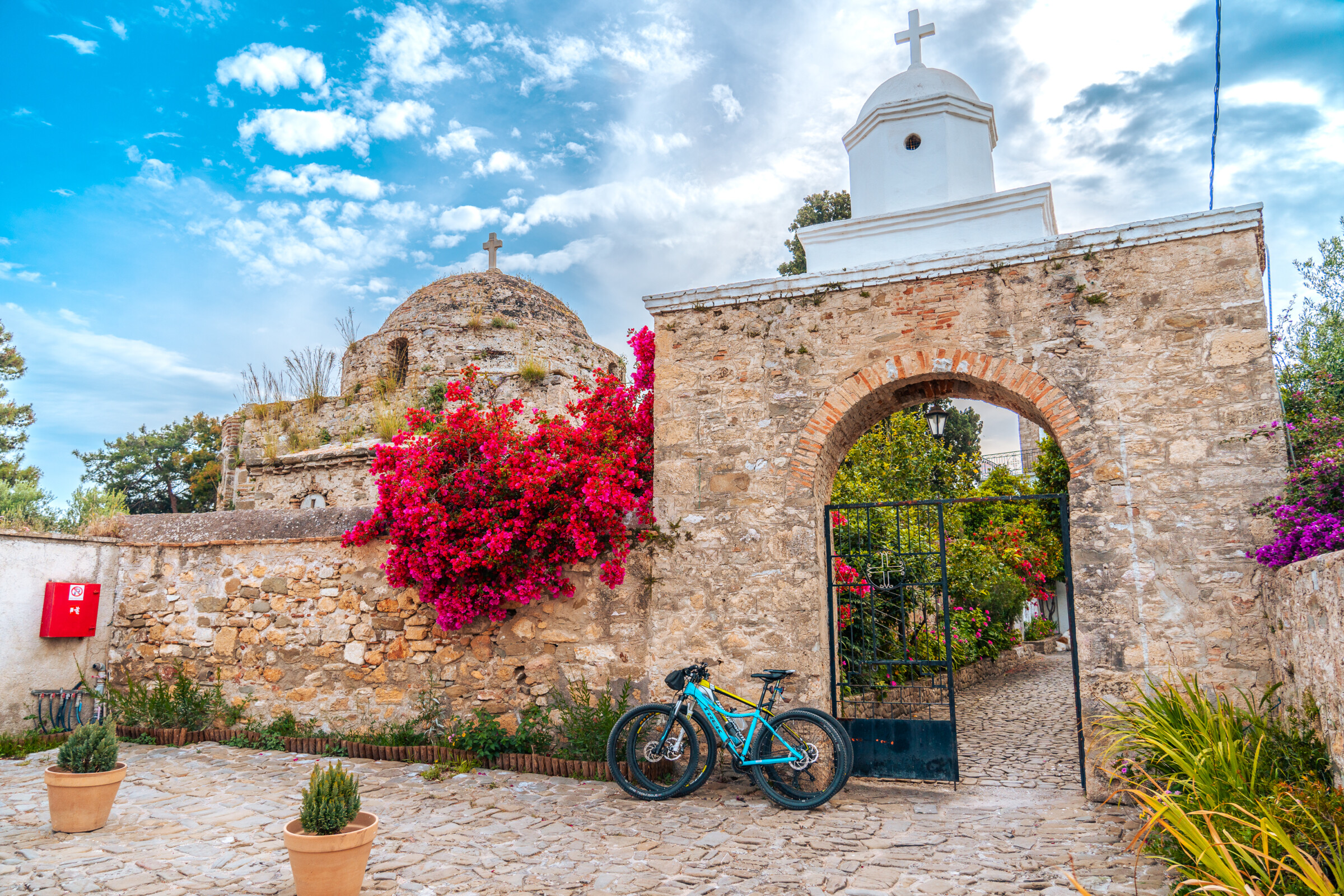 This image shows the castle gate with a brightly coloured bougainvillea. There are also two bicycles by the stone wall. 