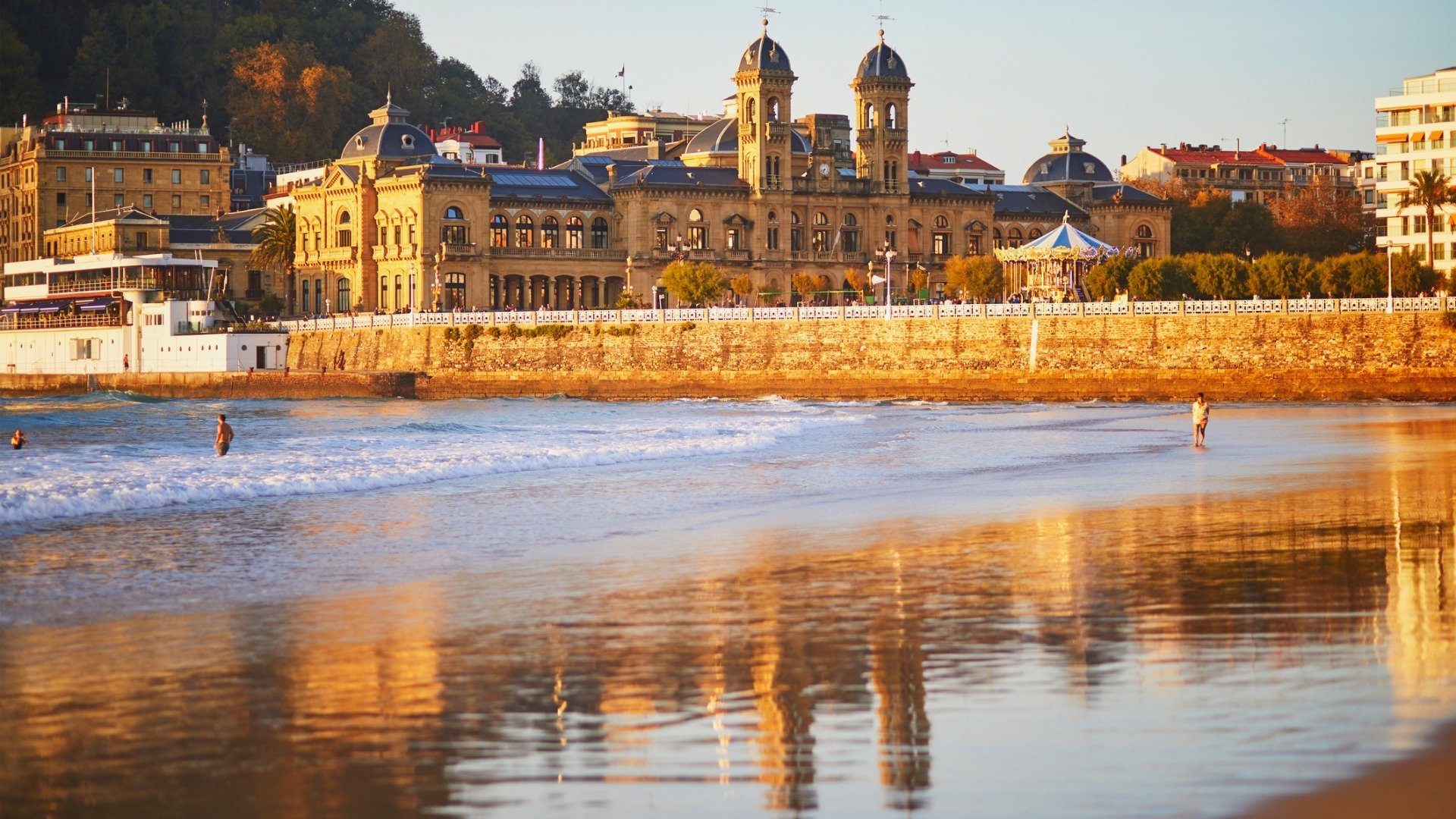La Concha Beach in the foreground with grand buildings in the background, all dyed in golden sunlight. 