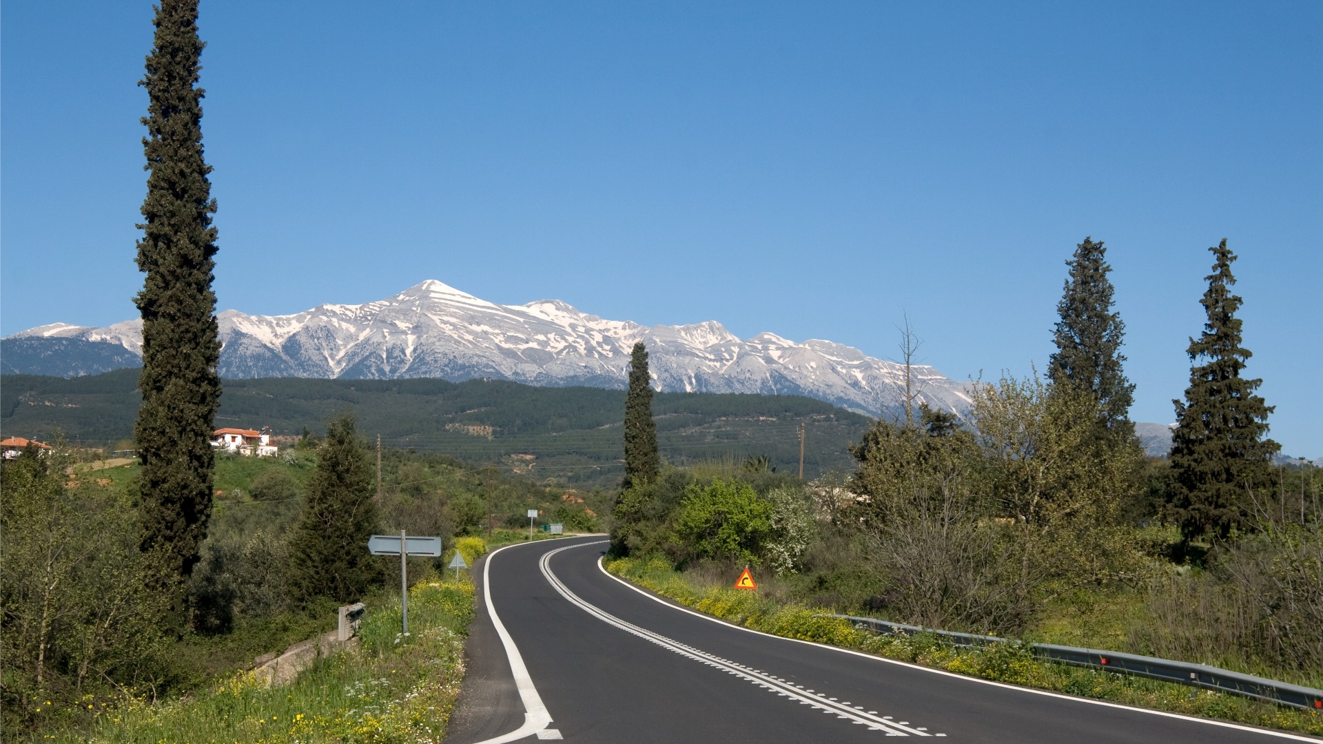 This image shows a road zigzagging through the countryside with snow-capped mountains in the background.