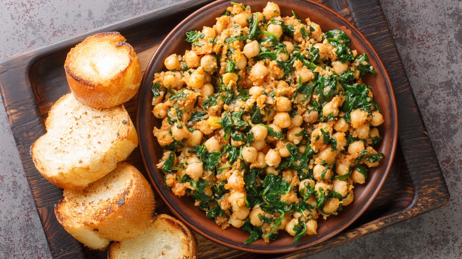 This is a dish of chickpeas with spinach with slices of bread next to it. 