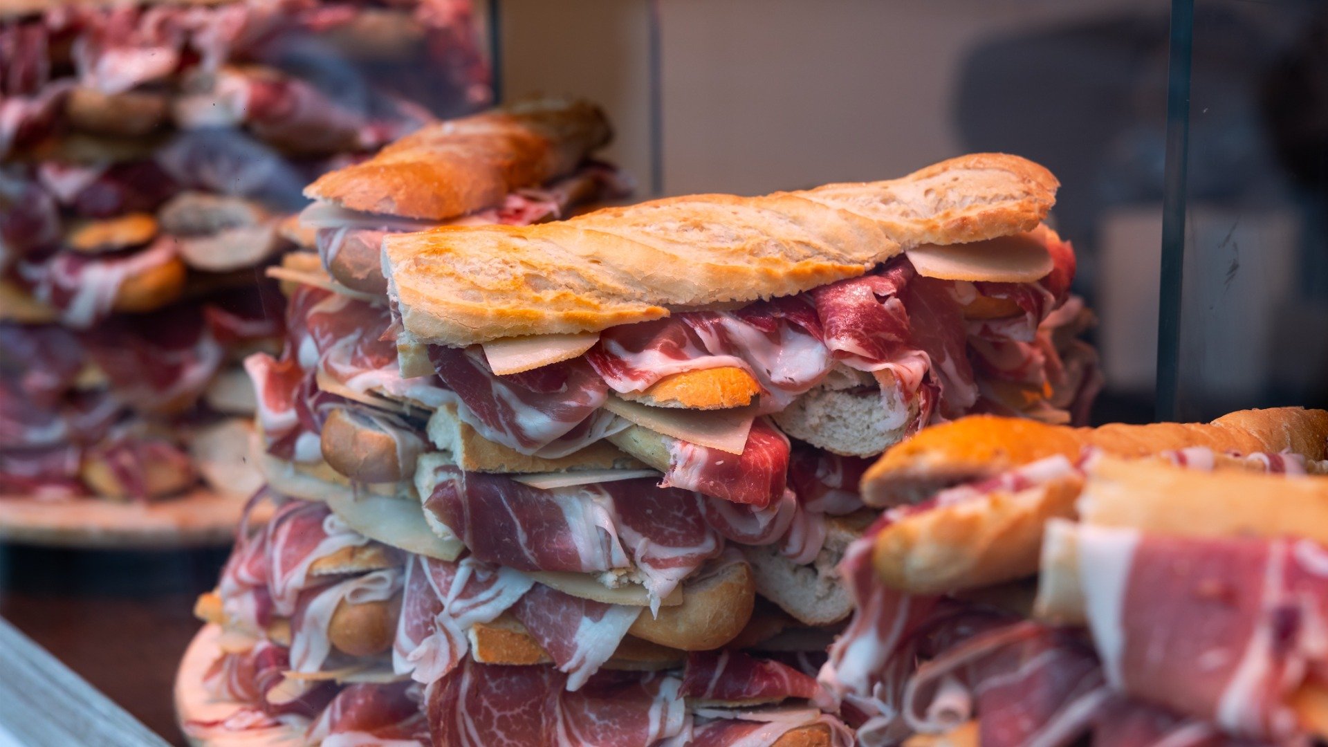 This image shows many bocadillos with jamon iberico stacked one on top of the other at a bar window. 